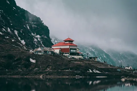 A red-roofed shrine on the shore of a still mountain lake under low cloud, near Gangtok, Sikkim