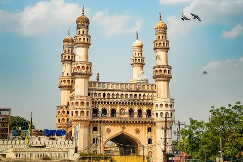 The four minarets of Charminar against a blue sky with pigeons in flight, Hyderabad