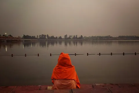 A person in an orange shawl sits at the edge of a large water tank at dusk in Kurukshetra
