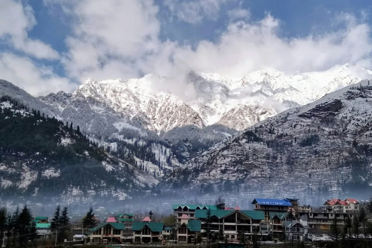 Snow-covered peaks above a village of green-roofed buildings in the Manali valley
